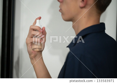 Holding a transparent spray bottle in a stylish indoor setting while preparing for a refreshing beauty routine during afternoon self-care 133583971