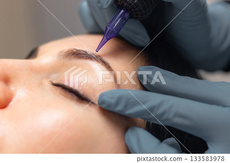 Close up of a cosmetologist performing eyebrow microblading on a female client. Professional beauty procedure, sterile tools, precision work and eyebrow shaping in a modern beauty studio. Close up of a cosmetologist performing eyebrow microblading on a female client. Professional beauty procedure, sterile tools, precision work and eyebrow shaping in a modern beauty studio. 133583978