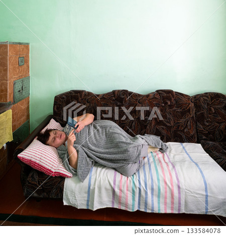 Comfortable moment spent on a cozy sofa scrolling through a smartphone while wrapped in a warm blanket in a softly lit living space Comfortable moment spent on a cozy sofa scrolling through a smartphone while wrapped in a warm blanket in a softly lit living space 133584078