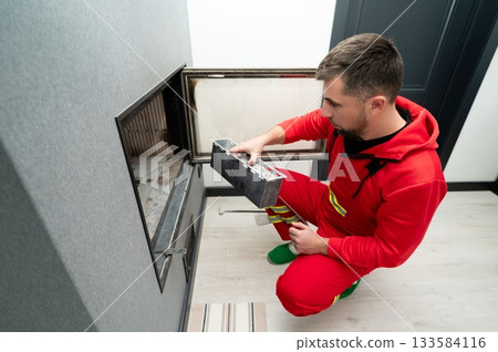 Skilled technician performs maintenance on modern fireplace in contemporary home during daylight hours to ensure safety and efficiency in heating Skilled technician performs maintenance on modern fireplace in contemporary home during daylight hours to ensure safety and efficiency in heating 133584116