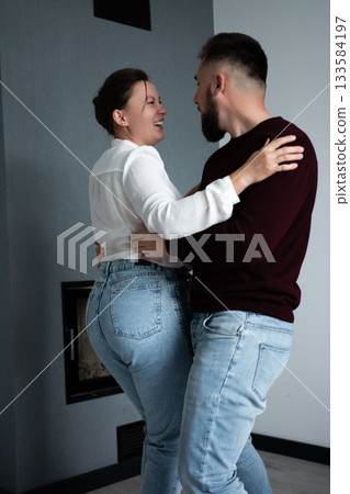 Couple enjoys a joyful dance together in a cozy living room, radiating love and happiness against a minimalist backdrop during a quiet evening Couple enjoys a joyful dance together in a cozy living room, radiating love and happiness against a minimalist backdrop during a quiet evening 133584197