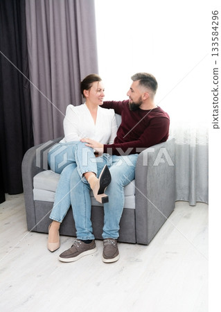 Couple enjoying intimate moments on a cozy sofa in a well-lit room, sharing smiles and laughter in an atmosphere of love and warmth Couple enjoying intimate moments on a cozy sofa in a well-lit room, sharing smiles and laughter in an atmosphere of love and warmth 133584296