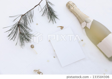 Festive winter flat lay. Champagne bottle, blank card, pine branch, golden star confetti on snowy background. Birthday celebration, New Year Party Invitation. Christmas holiday greeting mockup scene. 133584306