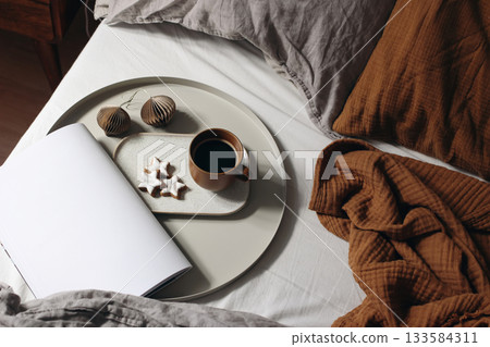 Christmas interior. Cozy morning in bed with coffee cup, star gingerbread cookies. Open book, magazine mockup. Muslin bedding, pillows. Winter mood, relaxing holiday home scene. Scandinavian top view Christmas interior. Cozy morning in bed with coffee cup, star gingerbread cookies. Open book, magazine mockup. Muslin bedding, pillows. Winter mood, relaxing holiday home scene. Scandinavian top view 133584311
