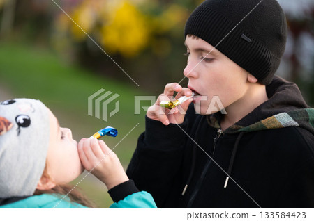 Joyful moments shared between siblings enjoying candy during a sunny day in the park, surrounded by vibrant flowers and laughter 133584423