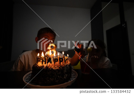 Surrounded by warmth and laughter, a child celebrates their eighth birthday with a chocolate cake adorned with candles and joyful memories in a cozy indoor setting 133584432