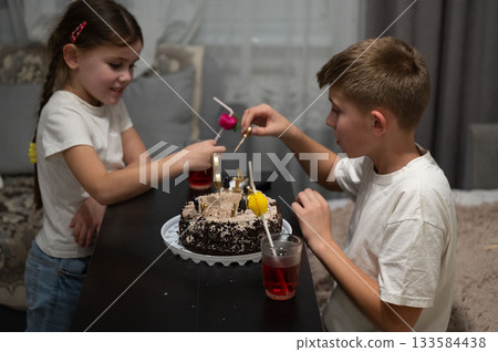 Kids celebrating with a cake in a cozy room filled with joy and laughter while enjoying a fun dessert decorating activity during a special occasion with a table setting at night Kids celebrating with a cake in a cozy room filled with joy and laughter while enjoying a fun dessert decorating activity during a special occasion with a table setting at night 133584438