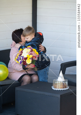Emotional embrace between mother and son celebrating a special day with flowers and decorations in a cozy outdoor setting on a sunny afternoon Emotional embrace between mother and son celebrating a special day with flowers and decorations in a cozy outdoor setting on a sunny afternoon 133584442