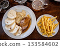 Prague, czech republic, august 9, 2023. Traditional czech meal featuring roasted pork, savory bread dumplings, sauerkraut, and a side of french fries, served in a pub 133584602