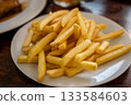 Prague, czech republic, august 9, 2023. Pile of crispy golden french fries on a white ceramic plate, side dish for fast food meal in a restaurant setting 133584603