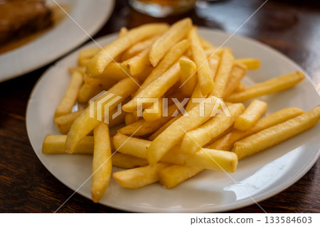 Prague, czech republic, august 9, 2023. Pile of crispy golden french fries on a white ceramic plate, side dish for fast food meal in a restaurant setting 133584603