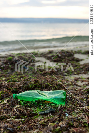 Volunteer picking up a green plastic bottle during beach cleanup, highlighting pollution, waste removal, and environmental protection. Volunteer picking up a green plastic bottle during beach cleanup, highlighting pollution, waste removal, and environmental protection. 133584653