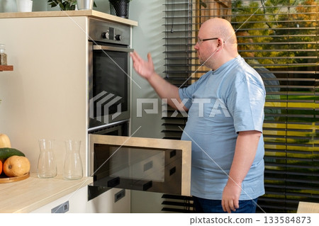 A man engaging with a modern oven within a stylish and contemporary kitchen environment 133584873
