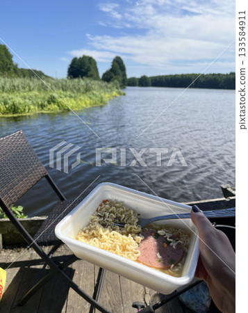 Instant noodles in plastic bowl by lake, outdoor camping lunch 133584911