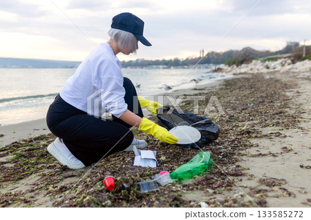Volunteer collecting plastic waste during beach cleanup, removing litter and protecting the shoreline environment. Volunteer collecting plastic waste during beach cleanup, removing litter and protecting the shoreline environment. 133585272