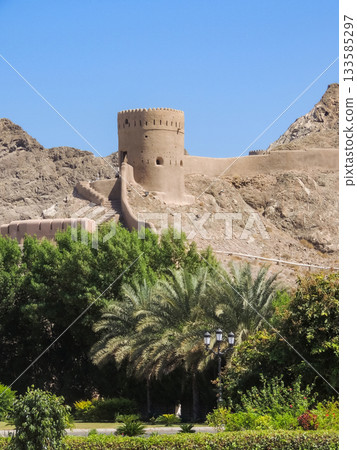 Historic watchtower and fort walls in Oman with palm trees 133585297