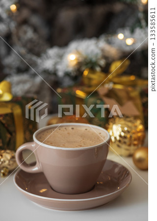 Cup of Hot Drink with Christmas Gifts and Ornaments in Cozy Holiday Setting against Christmas Tree and Lights 133585611