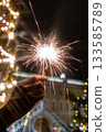 hand holding sparkler in front of Christmas tree. picture shows festive and joyful mood. 133585789