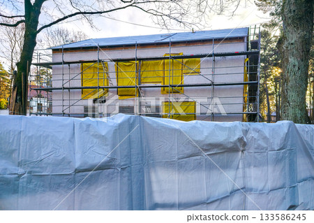 Construction site with scaffolding and plastic sheeting covering residential building renovation 133586245