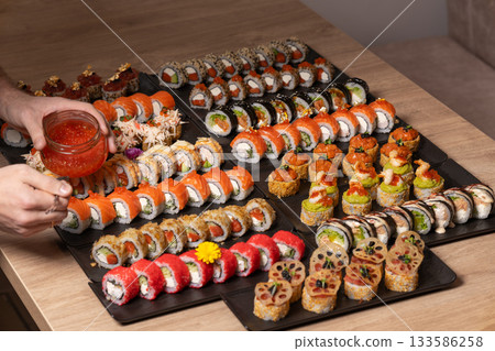 A person arranges a large, gourmet platter of diverse sushi and maki rolls 133586258