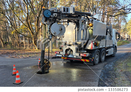 Hydro-vac sewer cleaning truck servicing underground pipeline through open manhole on a forest road 133586273