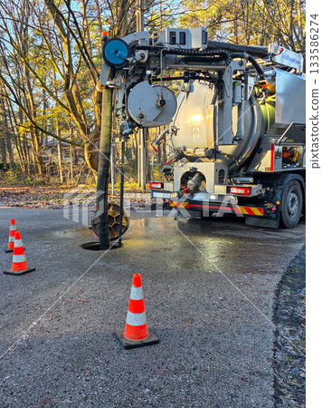 Sewer maintenance truck cleaning underground pipeline with vacuum hose and safety cones on roadway 133586274