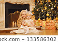 Happy children, little girls playing, gift box, Christmas tree, fireplace with holiday light at home 133586302