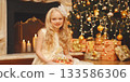 Happy little girl child with festive gift box sitting near Christmas tree and fireplace at home 133586306