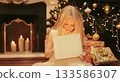 Happy little girl child with festive gift box sitting near Christmas tree and fireplace at home 133586307