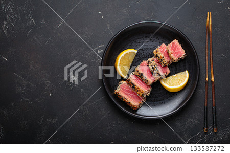 Seared grilled tuna steak tataki slices sesame seeds lemon black plate healthy delicacy space for text 133587272