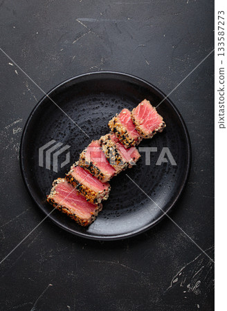 Seared grilled tuna steak tataki slices sesame seeds lemon black plate healthy delicacy Seared grilled tuna steak tataki slices sesame seeds lemon black plate healthy delicacy 133587273