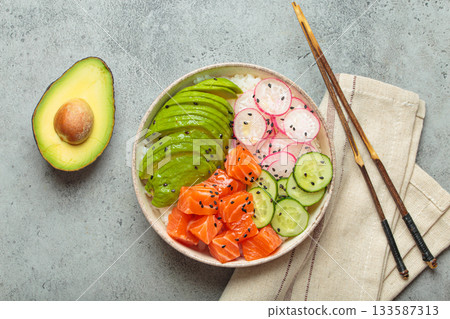Salmon poke bowl with avocado, radish, cucumber and rice on grey background top view 133587313