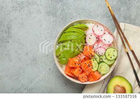 Salmon poke bowl with avocado, radish, cucumber and rice on grey background top view, space for text 133587316