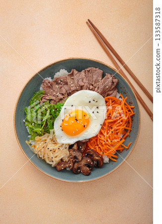 Traditional korean bibimbap with fried egg, beef and vegetables and other toppings top view on warm beige background 133587318
