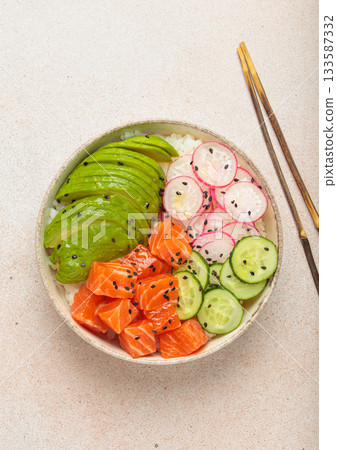 Salmon poke bowl with avocado, radish, cucumber and rice on light beige background top view 133587332