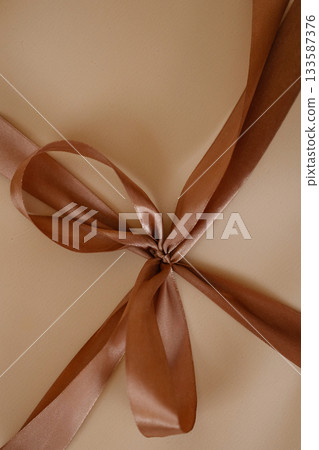 Brown satin ribbon bow on beige background 133587376
