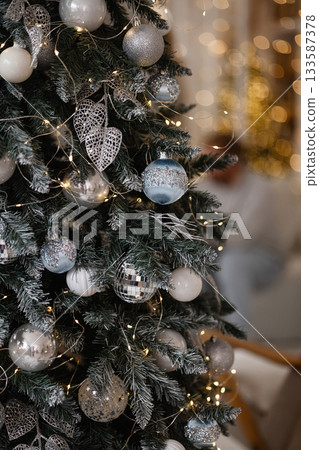Christmas tree with silver and blue ornaments and warm lights in cozy room Christmas tree with silver and blue ornaments and warm lights in cozy room 133587378