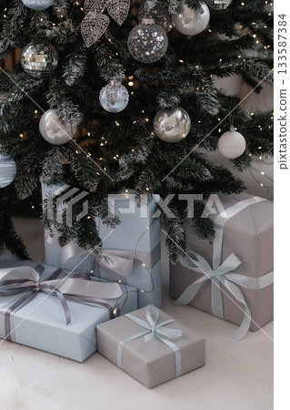 Christmas tree with silver ornaments and wrapped gifts on light floor Christmas tree with silver ornaments and wrapped gifts on light floor 133587384