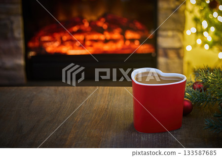 Cozy Hearthside Moment. Heart-shaped mug by a warm fireplace with holiday lights and a festive ambiance. Cozy Hearthside Moment. Heart-shaped mug by a warm fireplace with holiday lights and a festive ambiance. 133587685