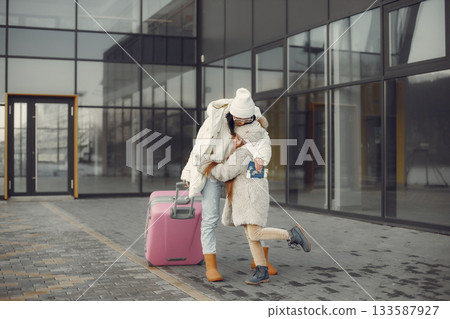 Mother and daughter come back from vacation. Brunette woman and girl with a luggage hugging near airport terminal. Mother and daughter wearing warm clothes. Mother and daughter come back from vacation. Brunette woman and girl with a luggage hugging near airport terminal. Mother and daughter wearing warm clothes. 133587927