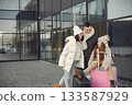 Family of three going on vacation. Man and girl sitting on a luggage and holding passports. Mother, father and daughter wearing warm clothes. 133587929