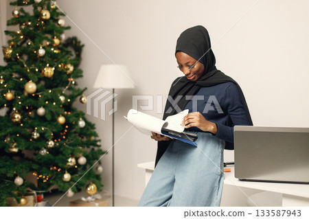 Young muslim business woman standing in her office. Woman holding documents. Woman wearing blue shirt and black hijab. Young muslim business woman standing in her office. Woman holding documents. Woman wearing blue shirt and black hijab. 133587943