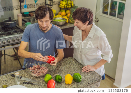 Man preparing lunch together with his elderly mother in an authentic modern kitchen, cutting ingredients and cooking a homemade meal in a warm family atmosphere, concept of family care and quality Man preparing lunch together with his elderly mother in an authentic modern kitchen, cutting ingredients and cooking a homemade meal in a warm family atmosphere, concept of family care and quality 133588176