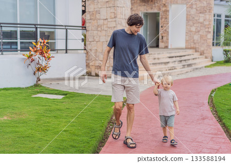 A man walking with his young son outdoors, holding hands and spending quality time together in a peaceful natural setting. Family bonding, parenting, childhood moments and healthy outdoor lifestyle A man walking with his young son outdoors, holding hands and spending quality time together in a peaceful natural setting. Family bonding, parenting, childhood moments and healthy outdoor lifestyle 133588194