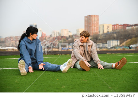 two women friends 50 and 60 years old doing bends forward sitting at a stadium, discussing two women friends 50 and 60 years old doing bends forward sitting at a stadium, discussing 133589457