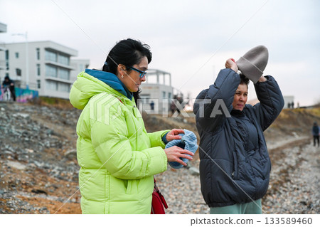 Two Russian women 50 years old and 60 years old walking in cold Vladivostok weather preparing for warmth putting on hats during a calm outdoor moment Two Russian women 50 years old and 60 years old walking in cold Vladivostok weather preparing for warmth putting on hats during a calm outdoor moment 133589460