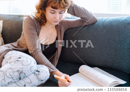 young woman at home writing notes in notebook while sitting on sofa 133589858