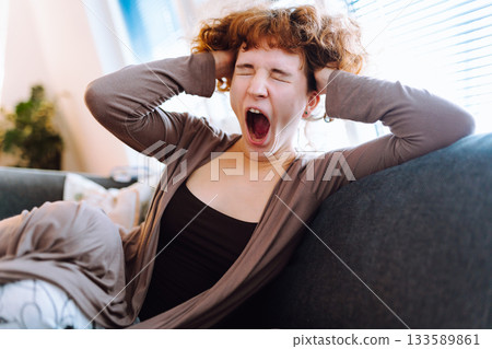 Portrait young woman yawning while sitting on sofa 133589861