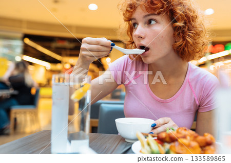 attractive redhead teen girl eating chinese soup in fast food restaurant 133589865