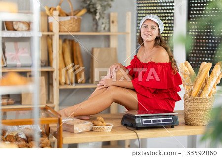 Playful young woman in red dress sitting on counter in bakery 133592060